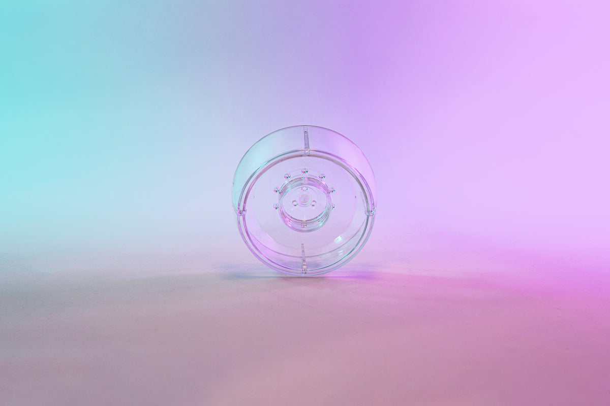 Clear plastic ring with interior smaller ring and holes for liquid to drain through. Set on a blue to purple gradient background.