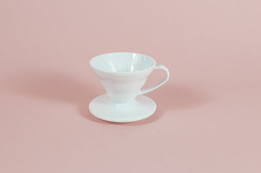 White all plastic cone shaped dripper with handle and round base on a pink backdrop.