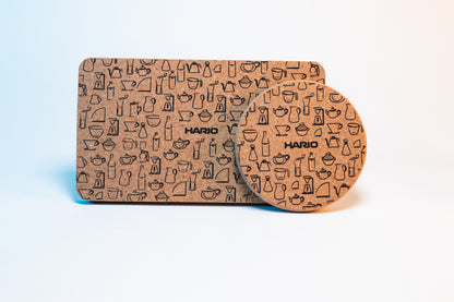 Rectangular cork coaster mat with black Hario logo and black pattern design of Hario products behind a circular cork coaster with black Hario logo and black pattern design of Hario products.