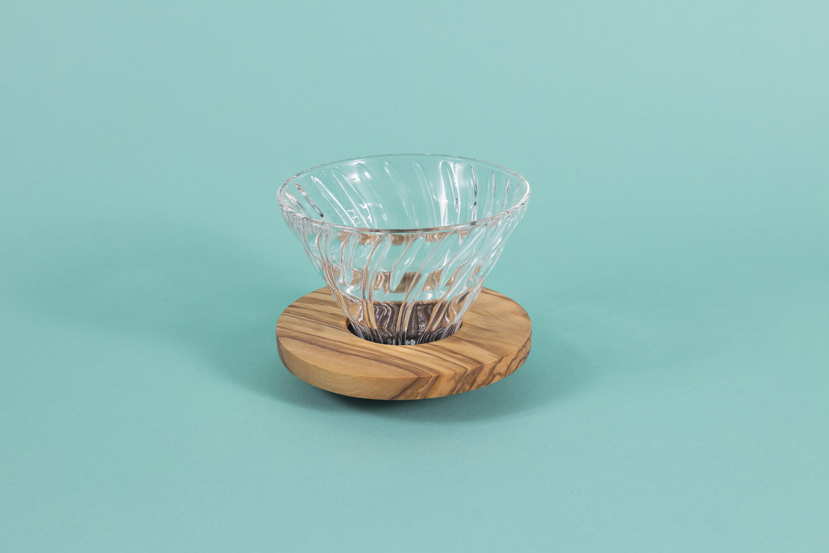 Clear all glass cone shaped coffee dripper with ribs, sitting in a round olive wood base.