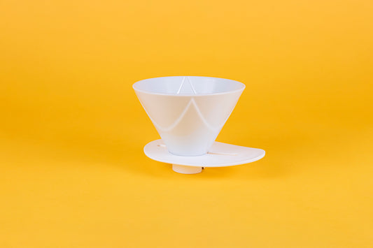 White plastic cone shaped dripper with Bézier ridges and oval shaped white plastic base on a yellow background.